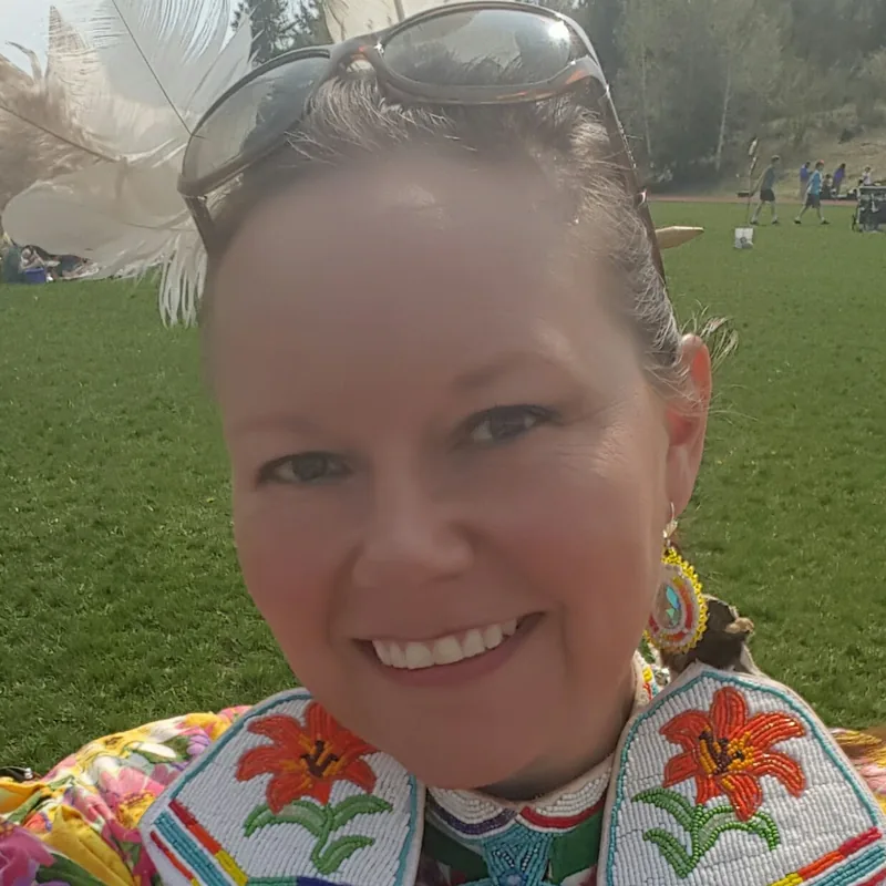 Robin Beauclair in regalia, wearing a floral beaded yoke and shoulder panels, on the grounds at a pow wow.